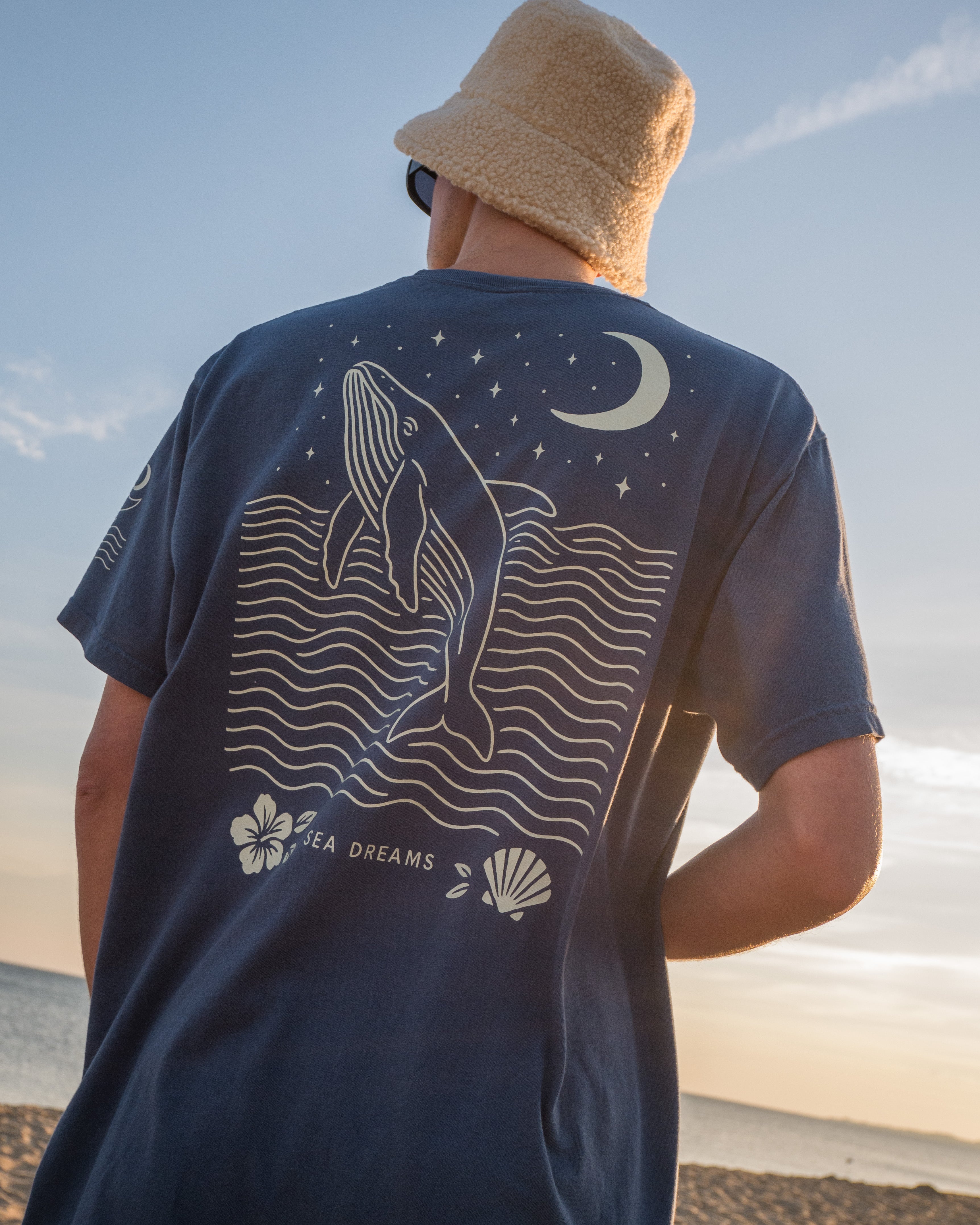 Person wearing a navy blue t-shirt with a whale design on the beach