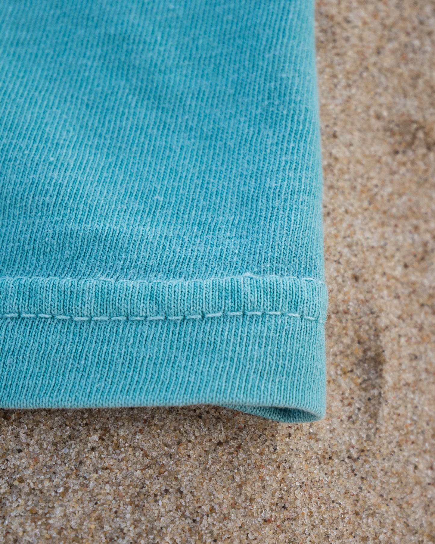 Close-up of a teal fabric edge on a sandy background