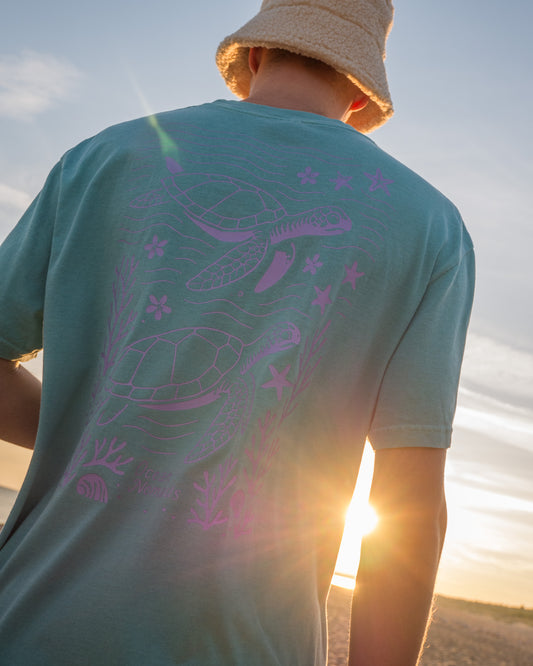 Person wearing a teal t-shirt with purple graphics at sunset
