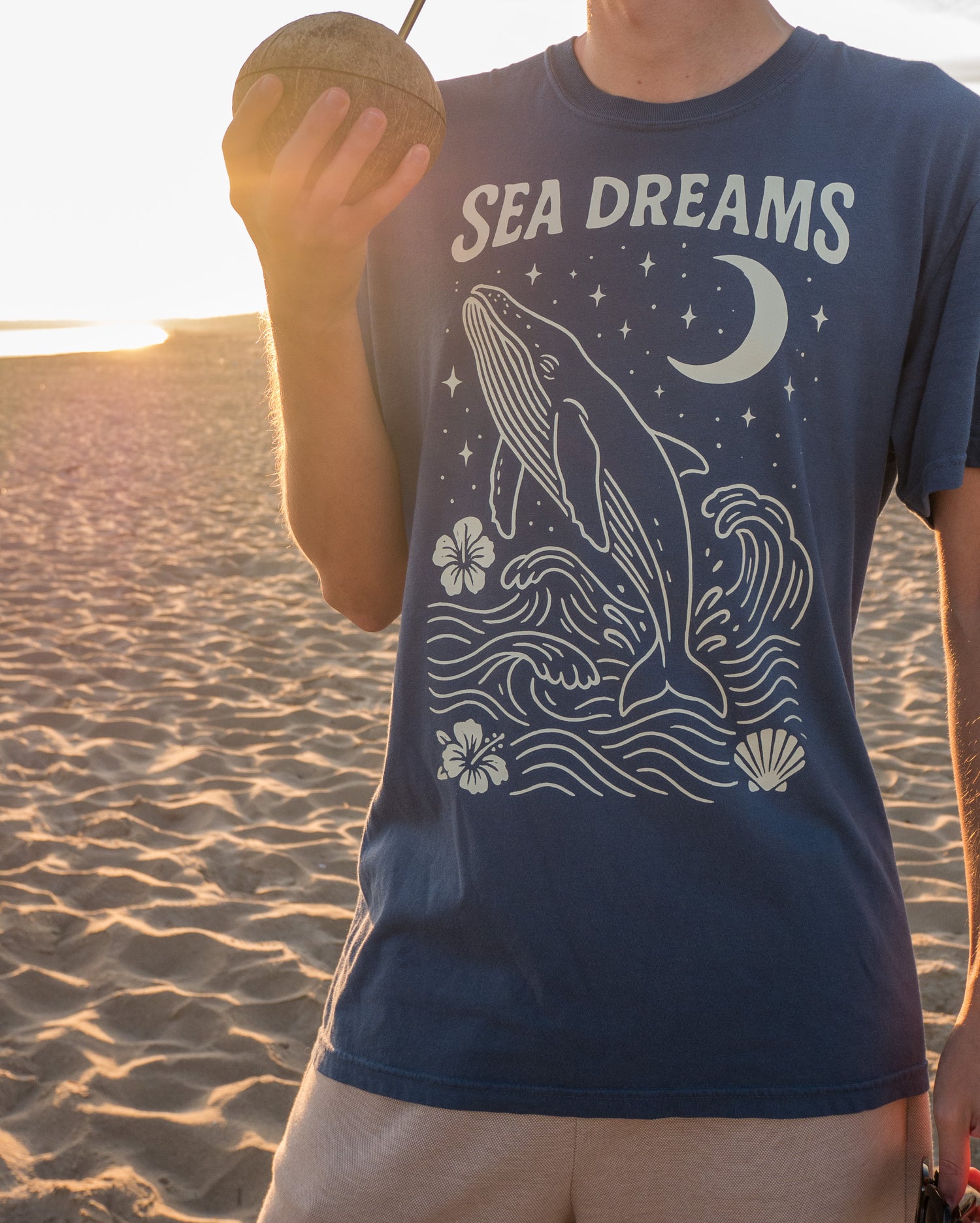Person wearing a blue t-shirt with a whale design and 'Sea Dreams' text on a beach.