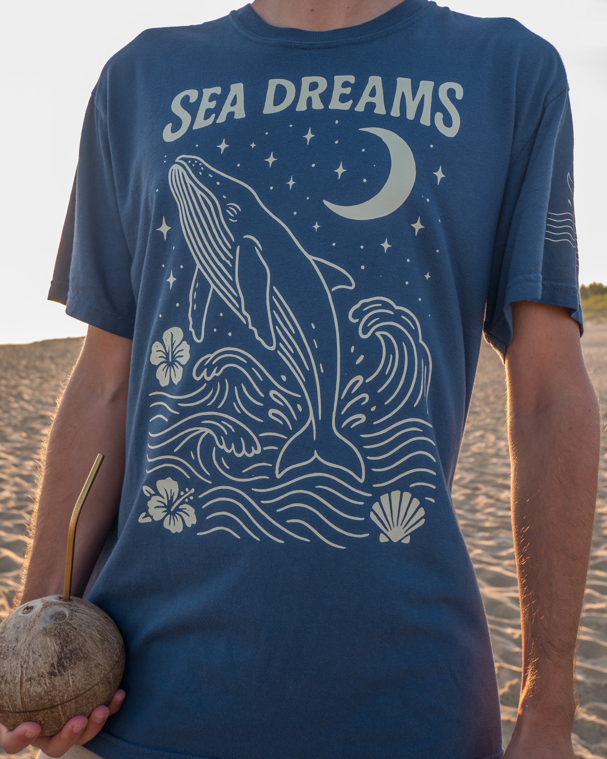 Person wearing a blue t-shirt with 'Sea Dreams' design on a beach