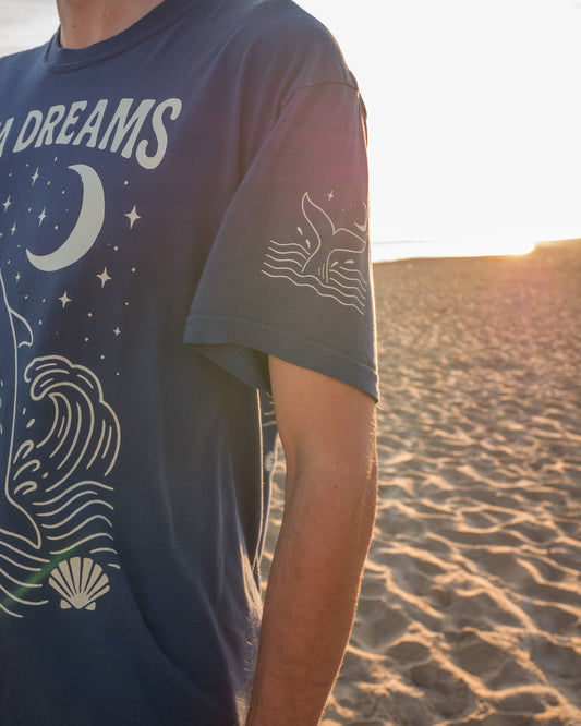 Person wearing a t-shirt with nature-themed designs on a beach at sunset.