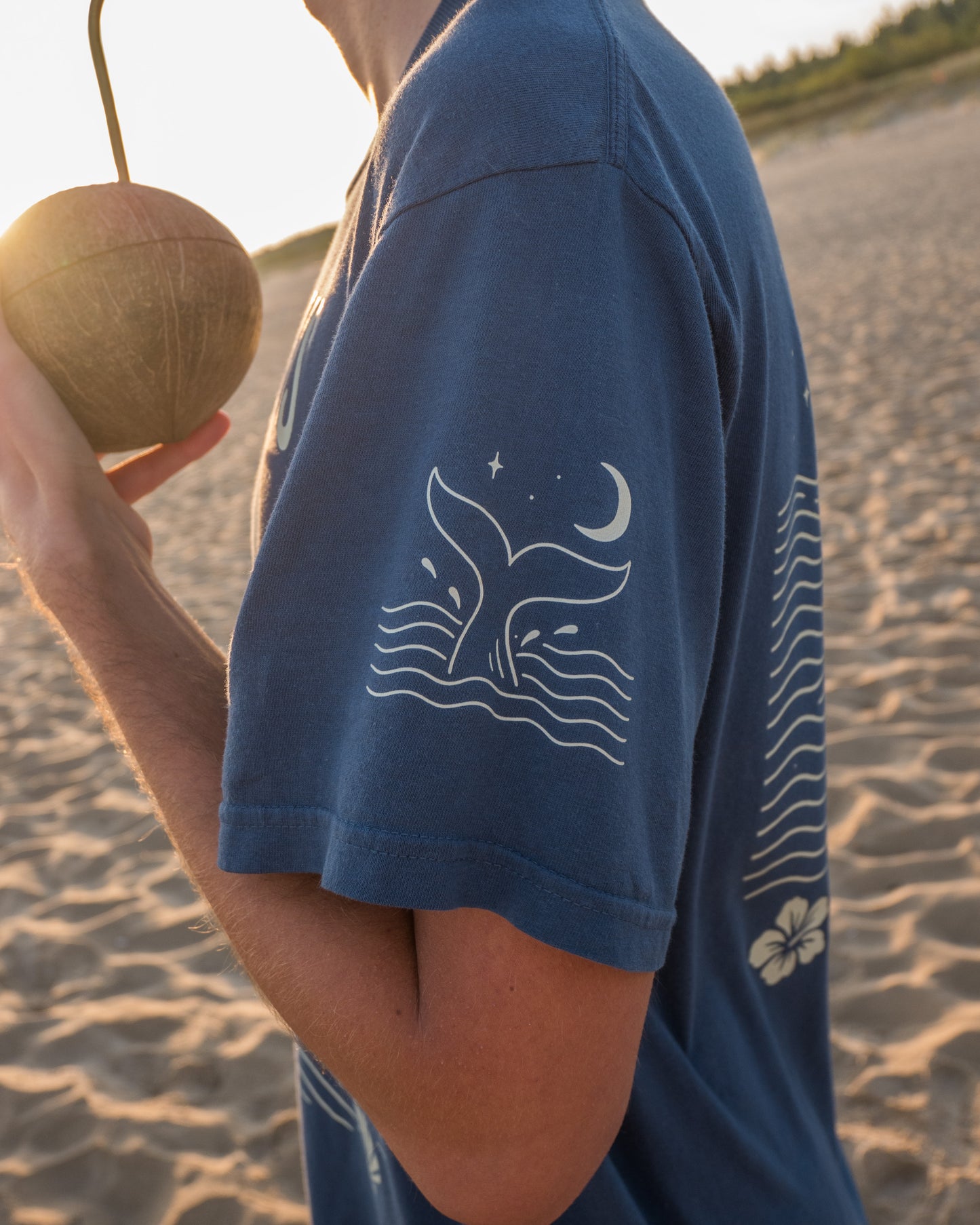 Person wearing a blue t-shirt with a whale design on a beach