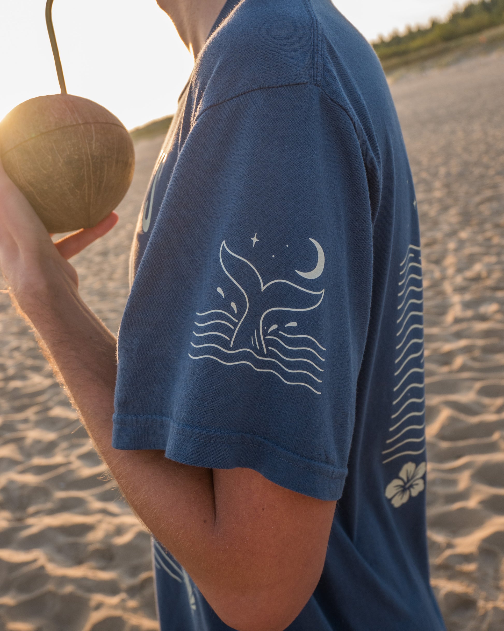 Person wearing a blue t-shirt with a whale design on a beach