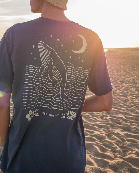 Person wearing a t-shirt with a whale design on a beach at sunset