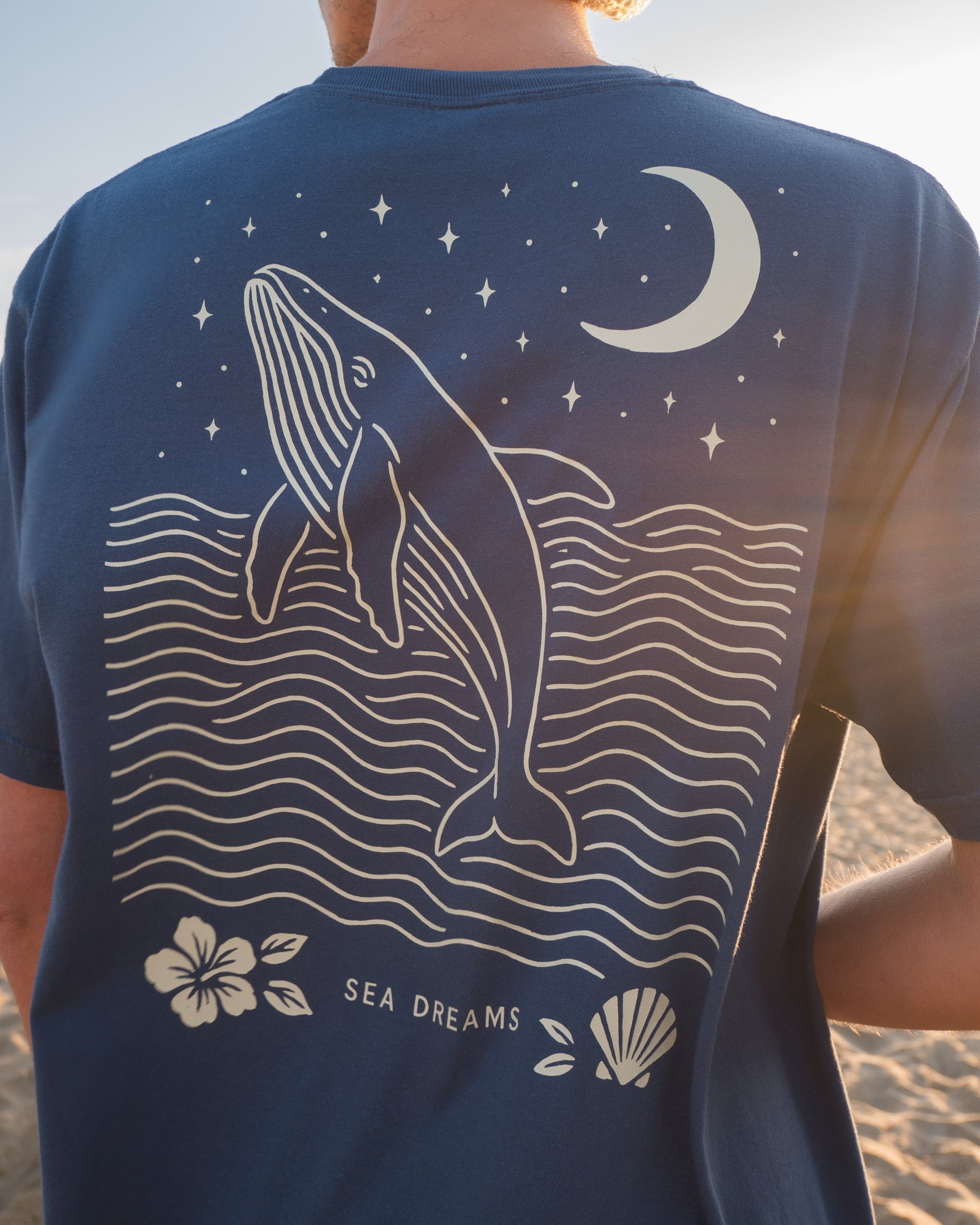 Navy blue t-shirt with a whale design and 'Sea Dreams' text on a beach.