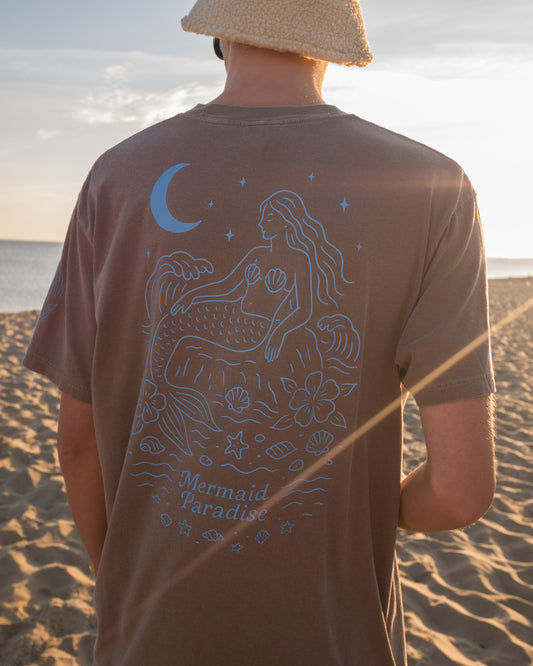 Person wearing a brown t-shirt with a mermaid design on a beach